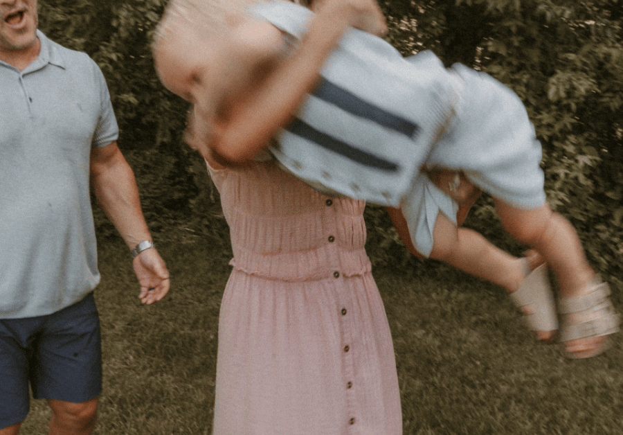 Parents swinging toddler boy in the air during playful backyard family photo session.