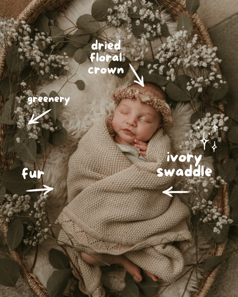 Newborn baby wrapped in ivory swaddle surrounded by greenery and dried baby’s breath flowers