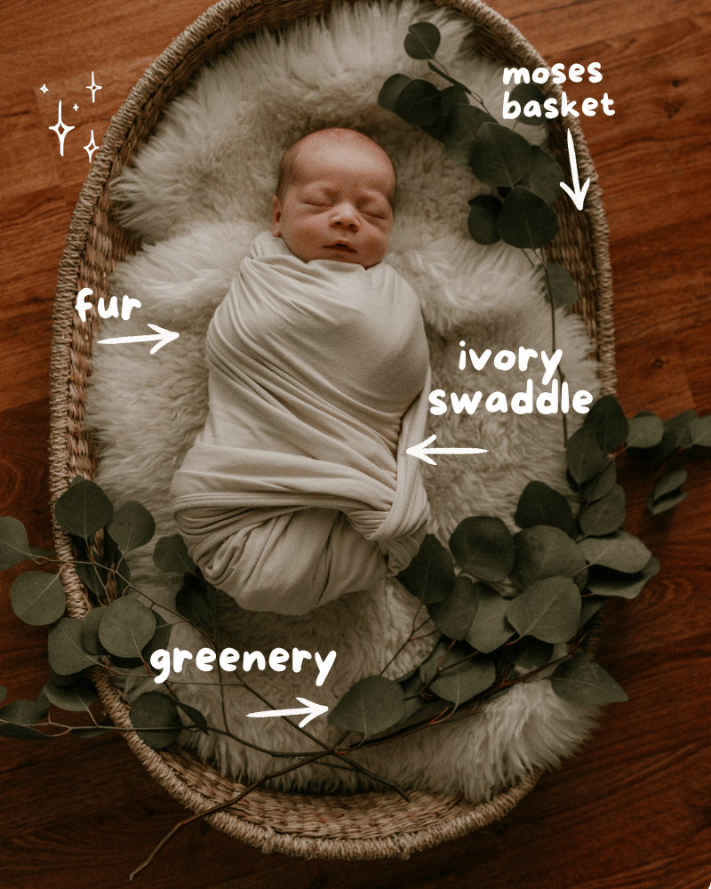 Newborn baby wrapped in ivory swaddle sleeping in a fur-lined moses basket with eucalyptus greenery on wood floor
