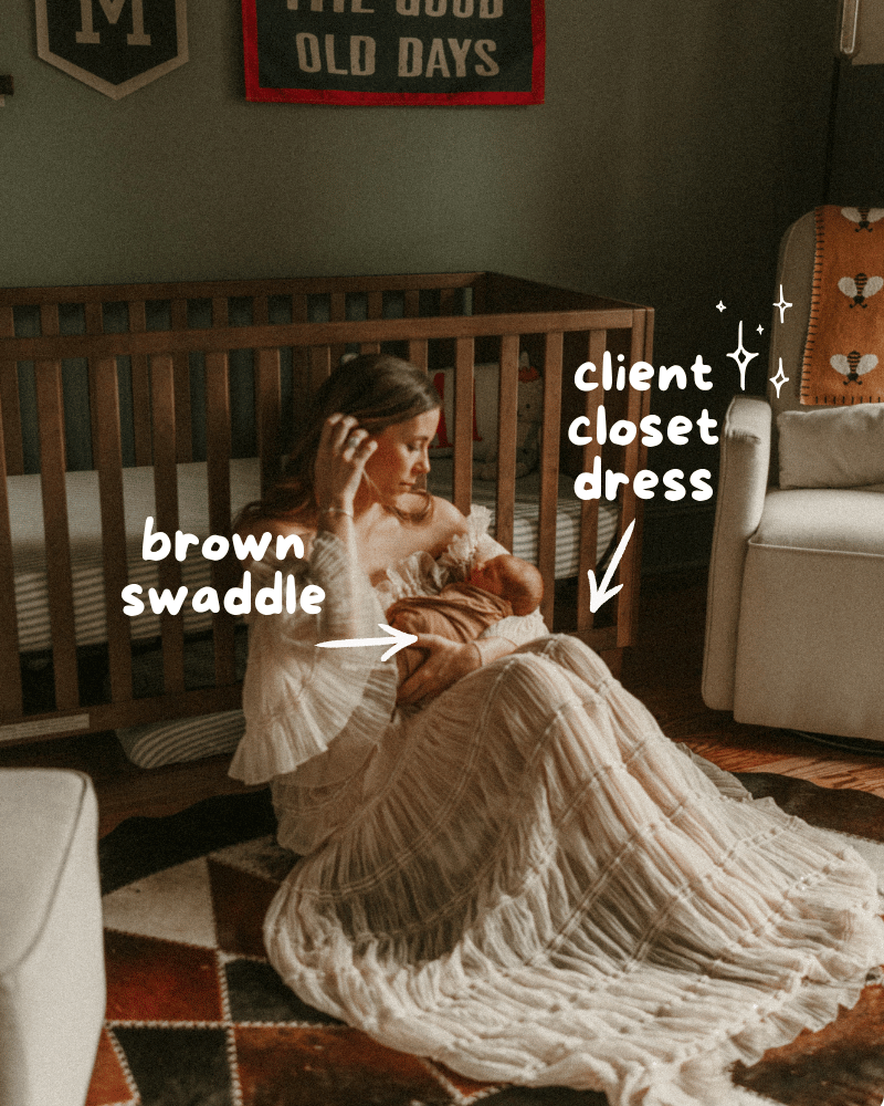 Mother in flowing white dress holding newborn in brown swaddle beside wooden crib