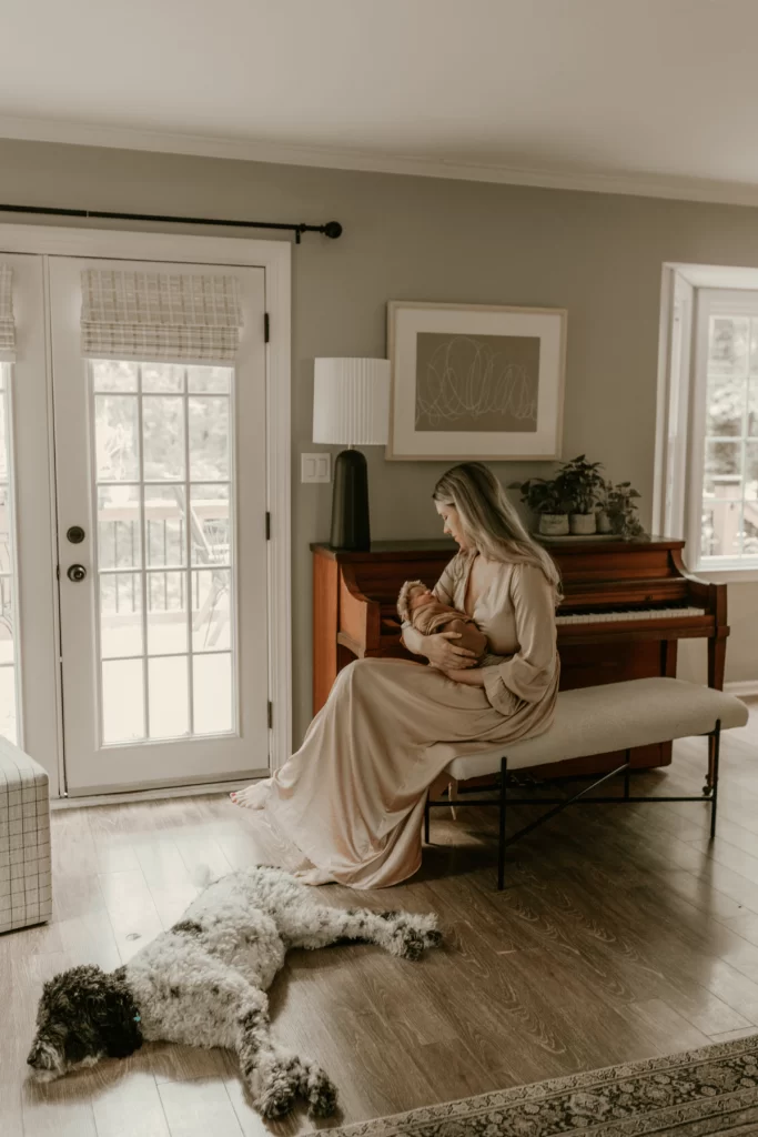New mom holding newborn on piano bench with dog laying nearby