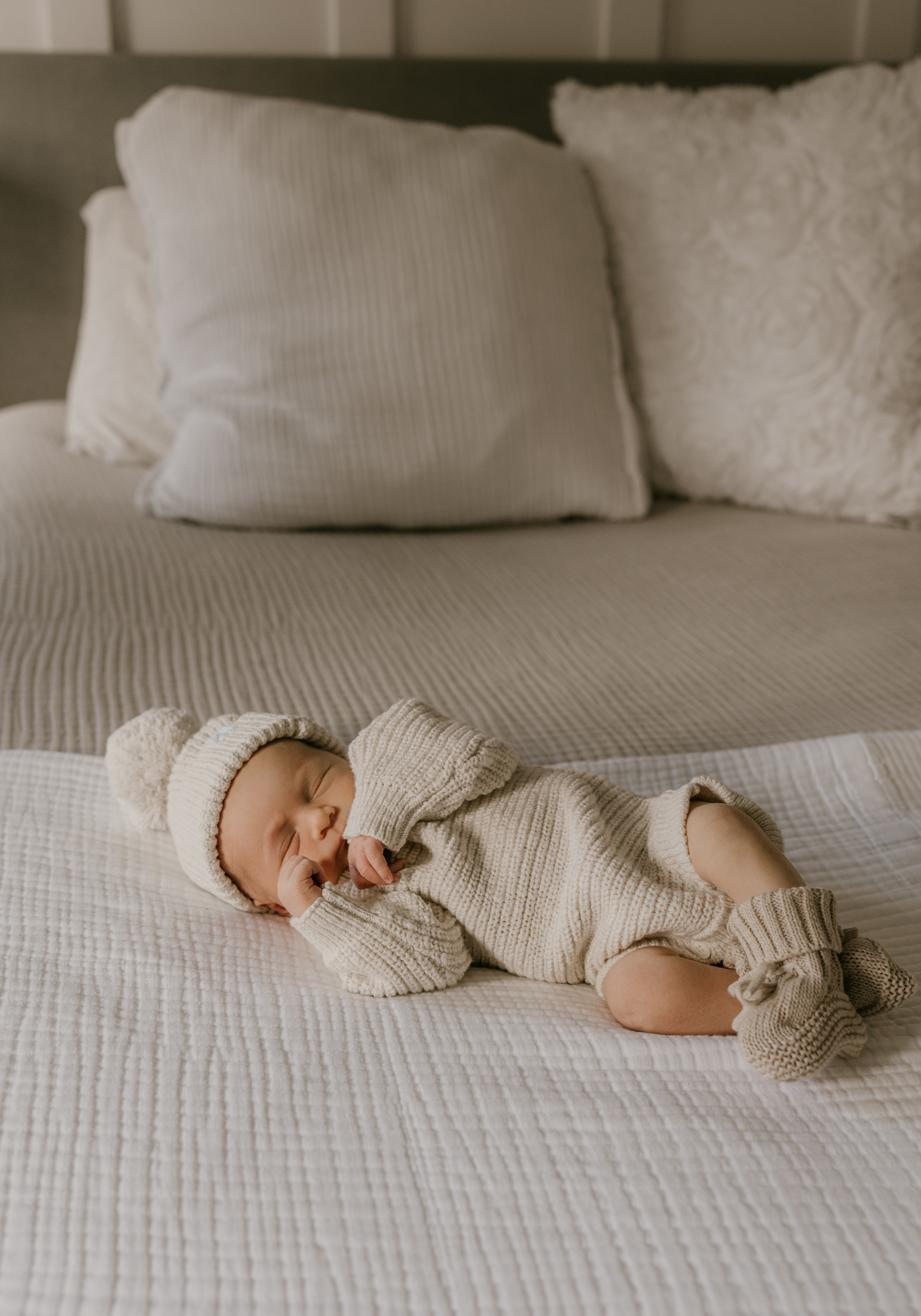 Newborn baby sleeping peacefully on a neutral bed in a cozy knit outfit and hat