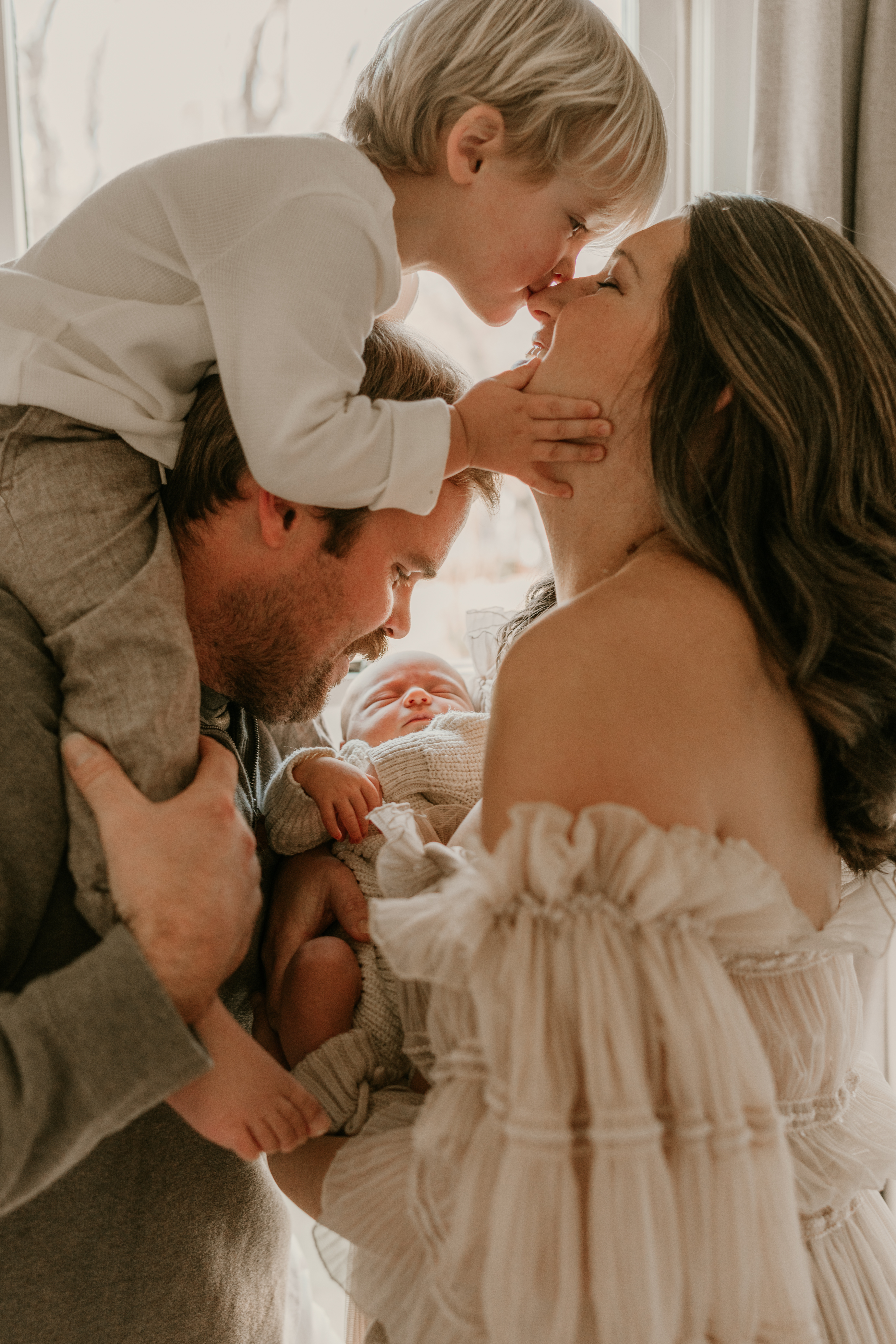 Toddler kisses mother’s nose while parents hold newborn baby during an at-home family session