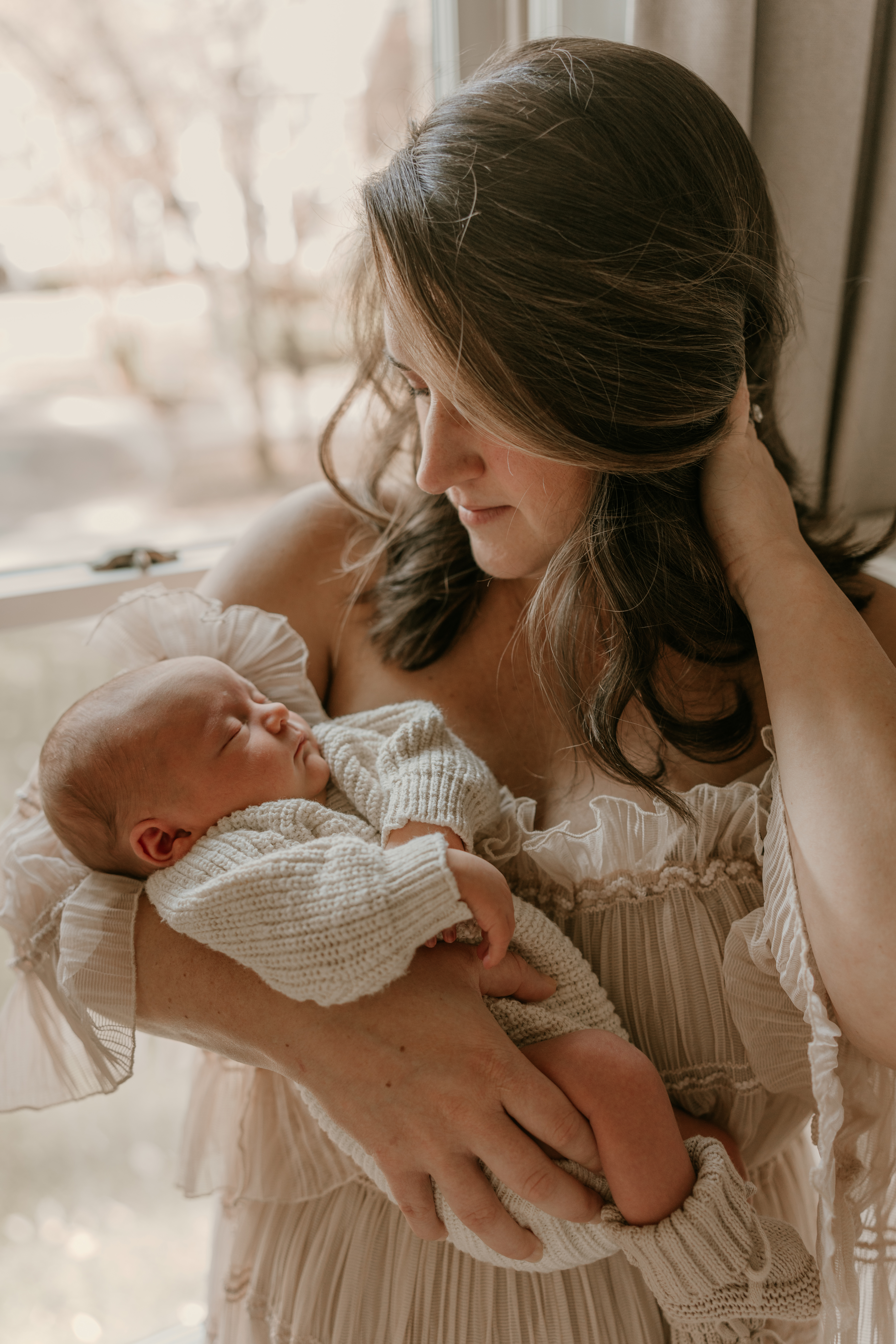Mother holding newborn baby in soft natural window light during lifestyle session