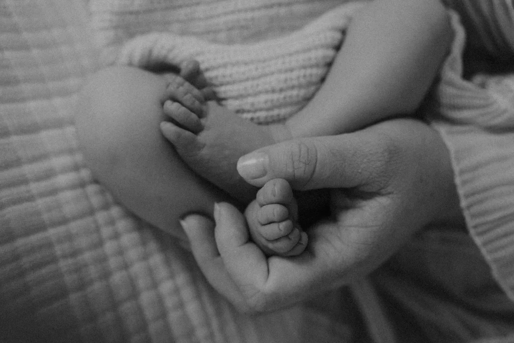 Close-up of newborn baby feet held gently in mother’s hand in black and white