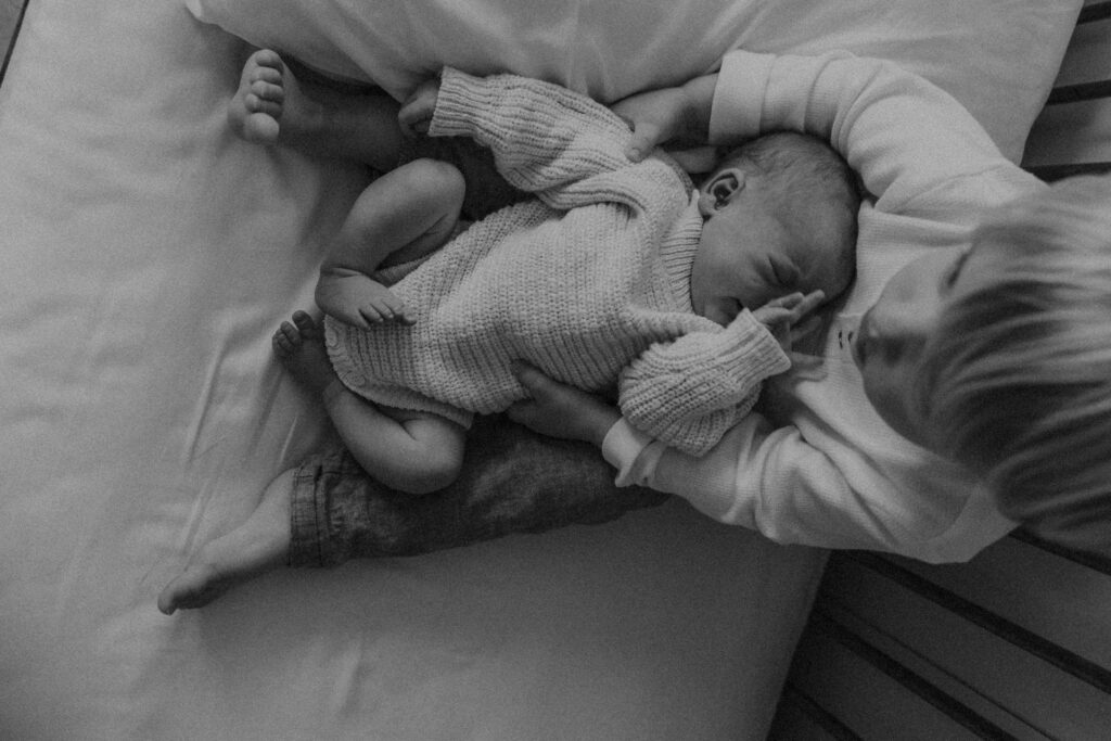 Black and white photo of toddler holding newborn sibling on a bed
