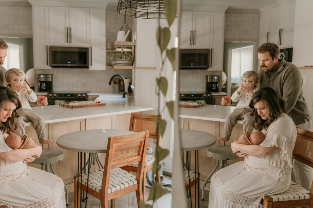 Family gathered in a warm, modern kitchen—mother cradling newborn, father helping toddler drink water