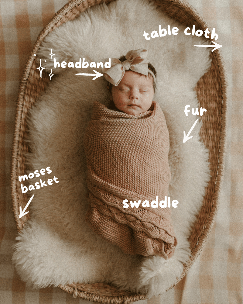 Newborn baby girl swaddled in pink blanket lying in a Moses basket with labeled photography props
