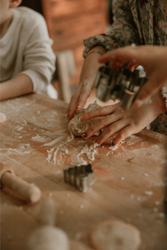 Child’s hands shaping cookie dough on floured surface with cookie cutters