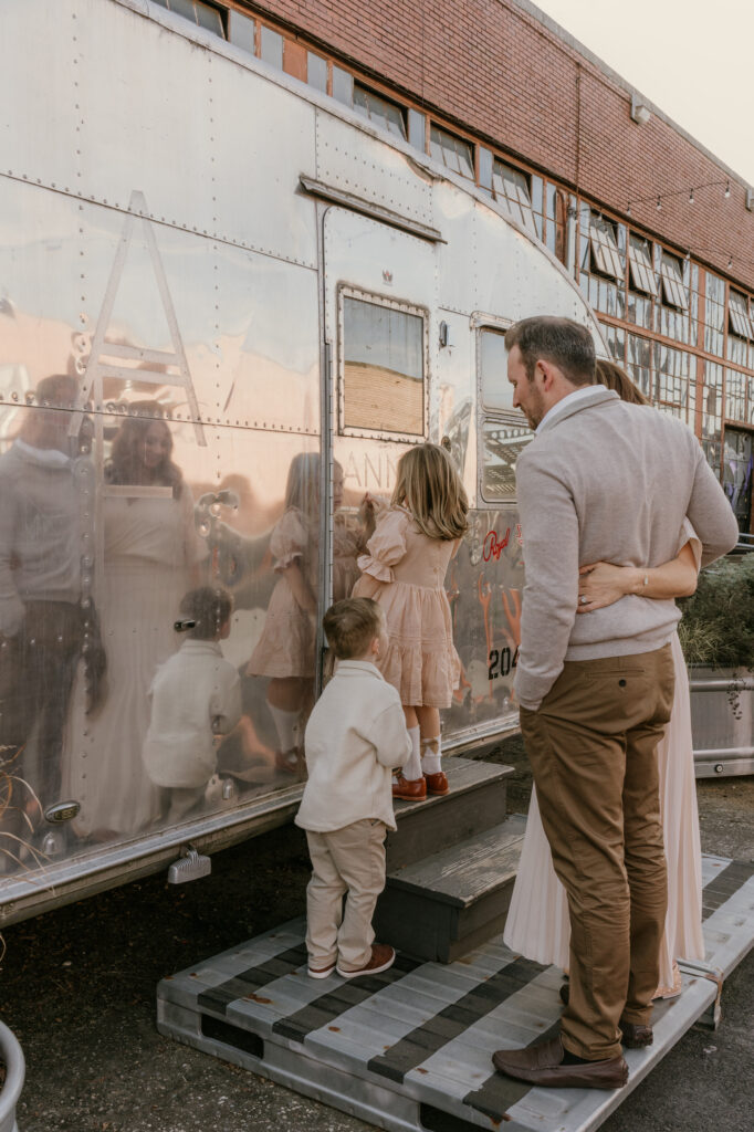 Family looking into the window of a vintage silver trailer at an outdoor market
