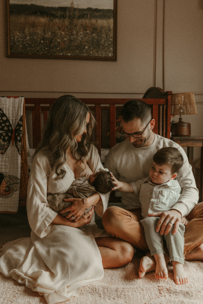 Toddler gently touching newborn while parents sit together during an in-home family session